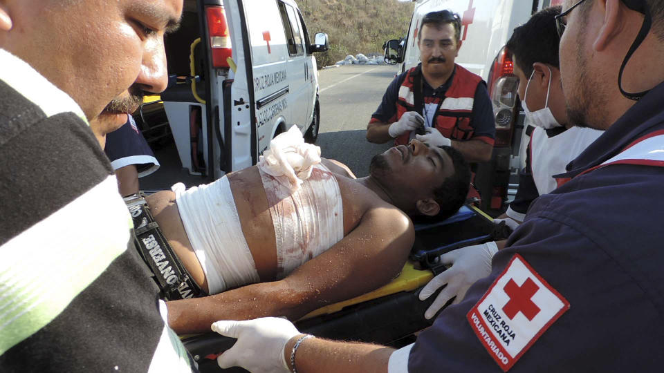 Emergency workers treat an injured man after a shootout with vigilantes fighting the Knights Templar cartel left five dead, at least two injured and several detained on the outskirts of the seaport of Lazaro Cardenas, western Mexico, Sunday April 27, 2014. Prosecutors in western Michoacan state confirmed Monday that the five dead belonged to a pseudo-vigilante group that had been financed by the gang to stem the advance of the self-defense movement. (AP Photo/Agencia Esquema)