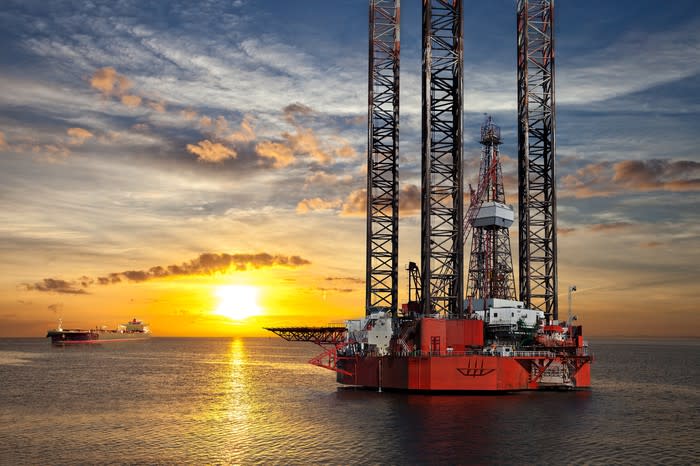 An offshore drilling rig and tanker with the sun setting in the background.