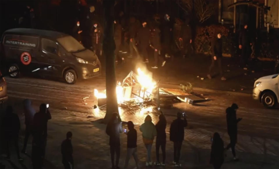 In this grab taken from video on Monday, Jan, 25, 2021, people use their phones to film items burning on a fire started by rioters, in Haarlem, Netherlands. Groups of youths have confronted police in several Dutch cities defying the country’s coronavirus curfew and throwing fireworks. Police in the port city of Rotterdam used a water cannon and tear gas in an attempt to disperse a crowd of rioters Monday night. (Mizzle Media via AP)