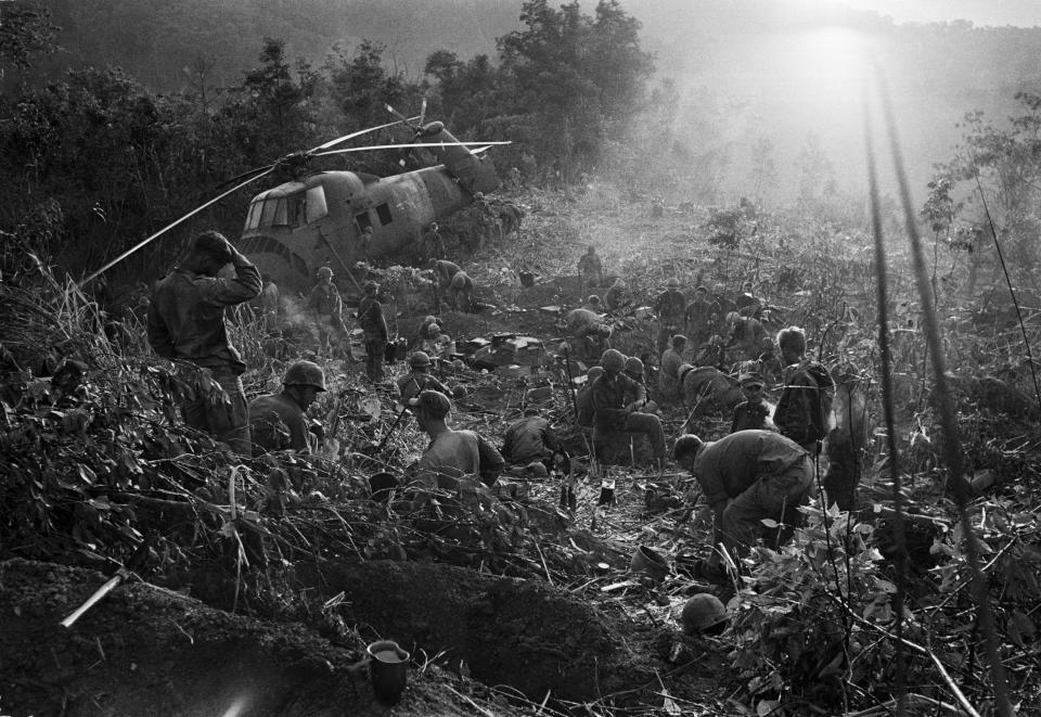 Weary after a third night of fighting against North Vietnamese troops, U.S. Marines crawl from foxholes located south of the demilitarized zone (DMZ) in Vietnam, September 1966. The helicopter at left was shot down when it came in to resupply the unit. (AP Photo/Henri Huet)