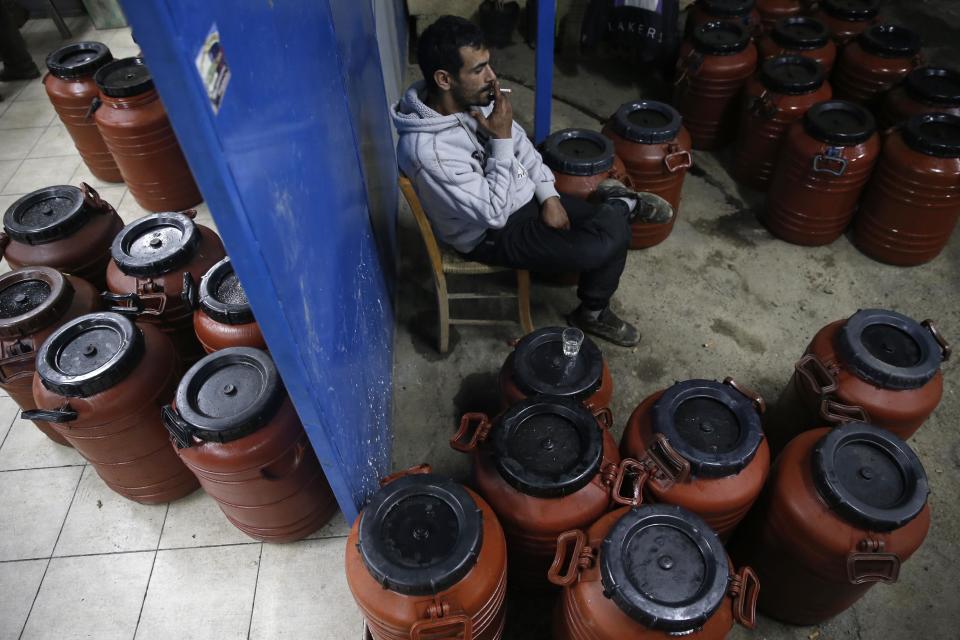 Carpenter Giorgos Karabatsis smokes a cigarette as he sits by 50-liter bulk containers at the entrance of a family-owned oil production plant in Velanidi village, 320 kilometers (200 miles) west of Athens, Greece on Thursday, Nov. 28, 2013. Karabatsis owns hundreds of olive trees and each year collects olives to help the income of his family. Widespread ownership of olive groves among Greeks has helped maintain supplies to households as they struggle through a sixth year of recession. (AP Photo/Petros Giannakouris)