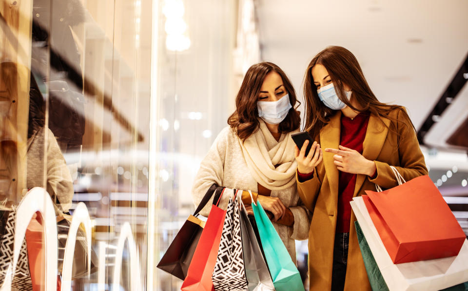 Two young girl friends in safety medical masks during shopping in the mall