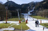 FILE - People ski up the slope on the Draxlhang in the Brauneck ski area using a T-bar lift in Lenggries, Germany, Wednesday, Dec. 28, 2022. Sparse snowfall and unseasonably warm weather in much of Europe is allowing green grass to blanket many mountaintops across the region where snow might normally be. It has caused headaches for ski slope operators and aficionados of Alpine white this time of year. (Sven Hoppe/dpa via AP, File)