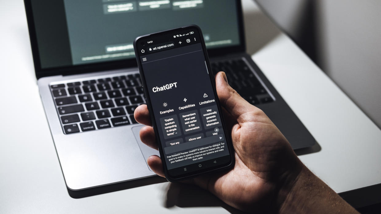  A hand holding a phone running ChatGPT in front of a laptop. 