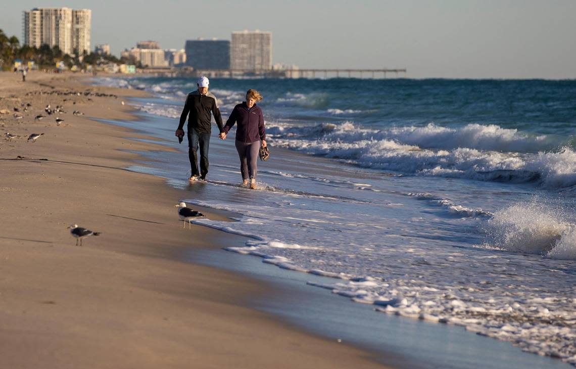 Jason Rayburn and Natalie Suiter walk near the shoreline as temperatures dip into the mid 40s on Saturday, Jan. 14, 2023, in Hollywood, Fla.