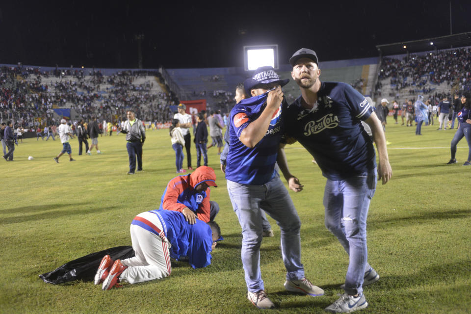 Soccer fans gather on the field in an attempt to escape tear gas that was fired by police who were trying to break up a deadly fight between fans before the start of a game between Motagua and Olimpia, at the national stadium in Tegucigalpa, Honduras, late Saturday, Aug. 17, 2019. The fight between fans of rival soccer teams outside the stadium left three people dead and led to the suspension of the game. (Victor Colindres/La Tribunal via AP)