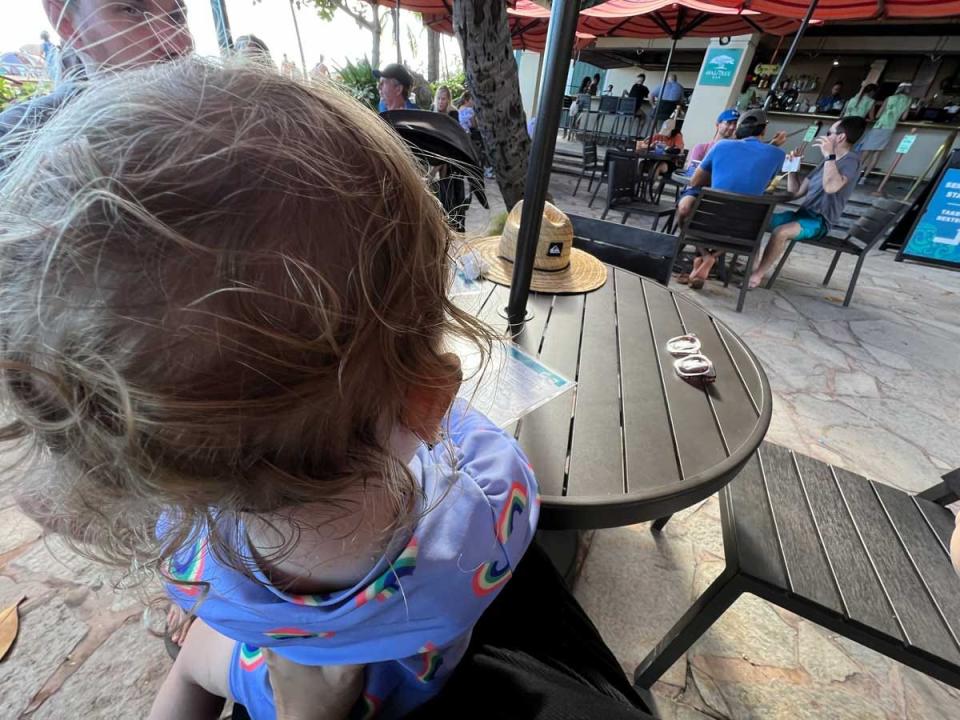 The top of a child's head who is sitting at an outdoor dining table.
