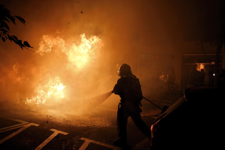 A firefighter tries to put off a fire on the street during clashes between protestors and police in Barcelona, Spain, Wednesday, Oct. 16, 2019. Spain's government said Wednesday it would do whatever it takes to stamp out violence in Catalonia, where clashes between regional independence supporters and police have injured more than 200 people in two days. (AP Photo/Emilio Morenatti)