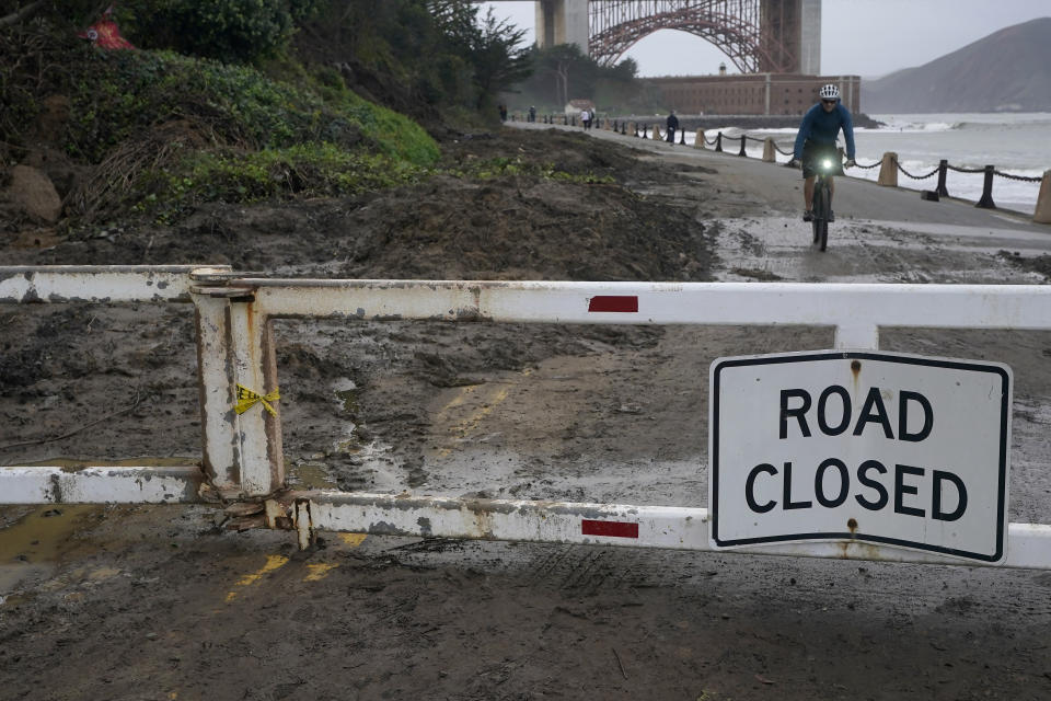 A bicyclist rides near mud and debris on a closed road near Fort Point in San Francisco, Friday, Jan. 6, 2023. California weather calmed Friday but the lull was expected to be brief as more Pacific storms lined up to blast into the state, where successive powerful weather systems have knocked out power to thousands, battered the coastline, flooded streets, toppled trees and caused at least six deaths. (AP Photo/Jeff Chiu)