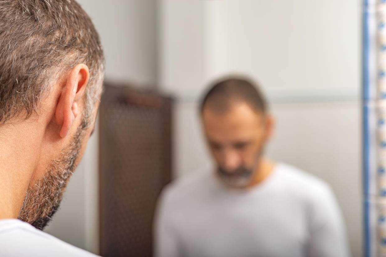 Spain: Blurry reflection in bathroom mirror of a man looking down. Concept: Erectile dysfunction, prostate problems, aging.