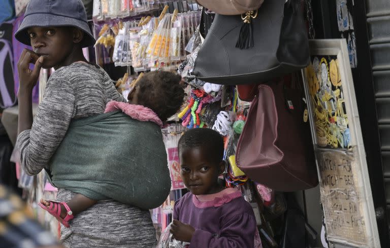 FILE — An unmasked woman with two kids walks through the busy Bara Taxi Rank in Soweto, South Africa, Tuesday, April 5, 2022. South Africa's health minister says it is likely the country has entered a new wave of COVID-19 earlier than expected as new infections and hospitalizations have risen rapidly over the past two weeks. (AP Photo/Thoko Chikondi/File)