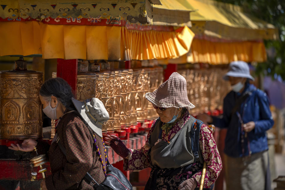 Members of the Buddhist faithful spin prayer wheels outside the Potala Palace in Lhasa in western China's Tibet Autonomous Region, Tuesday, June 1, 2021, as seen during a government organized visit for foreign journalists. High-pressure tactics employed by China's ruling Communist Party appear to be finding success in separating Tibetans from their traditional Buddhist culture and the influence of the Dalai Lama. (AP Photo/Mark Schiefelbein)