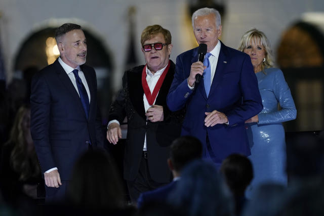 President Joe Biden speaks as David Furnish, husband of Elton John, left, Elton John and first lady Jill Biden listen after Biden presented him with a National Humanities Medal after a concert on the South Lawn of the White House in Washington, Friday, Sept. 23, 2022. (AP Photo/Susan Walsh)