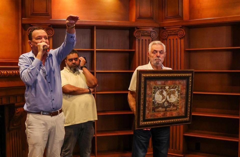 Charles Grasso holds a framed world map been auctioned by George Farley (far left) and Sam Abdoel, with Auctions4America on Saturday, Dec. 23, 2023, to people interested in buying a piece of La Maison Blanche —the White House — a 1930s neoclassical estate on the Intracoastal in Fort Lauderdale that will be demolished after the auction and replaced by a 20,000-square-foot modernist home.