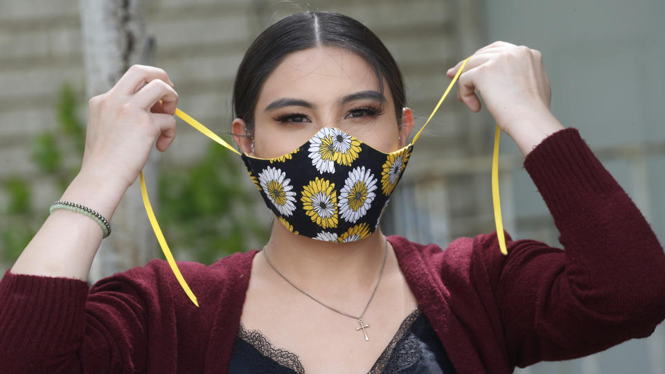 In this Monday, May 18, 2020, photo, Anissa Archuleta wears her mask at her home in Midvale, Utah. Jaime Ortega and her two daughters Anissa Archuleta and Alexis Archuleta had to get tested and be monitored for two weeks after they stopped by a birthday party for a young cousin whose father unknowingly had the new coronavirus. The women all tested negative, but received daily calls from health investigator Maria DiCaro to check on their symptoms. (AP Photo/Rick Bowmer)
