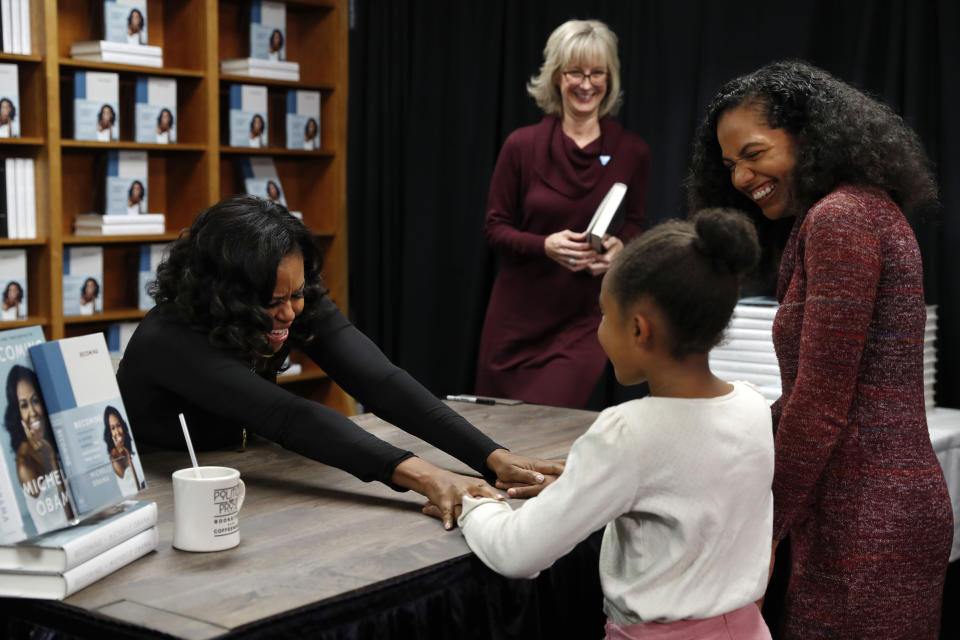 Former first lady Michelle Obama holds hands with Kaitlyn Saunders, 8, next to her mother Katrice Saunders, of Washington, after the 8-year-old told Obama how inspired she is by her and how she is a competitive figure skater, as they buy signed copies of Obama's book, "Becoming," Monday Nov. 18, 2019, at Politics and Prose Bookstore in Washington. (AP Photo/Jacquelyn Martin)