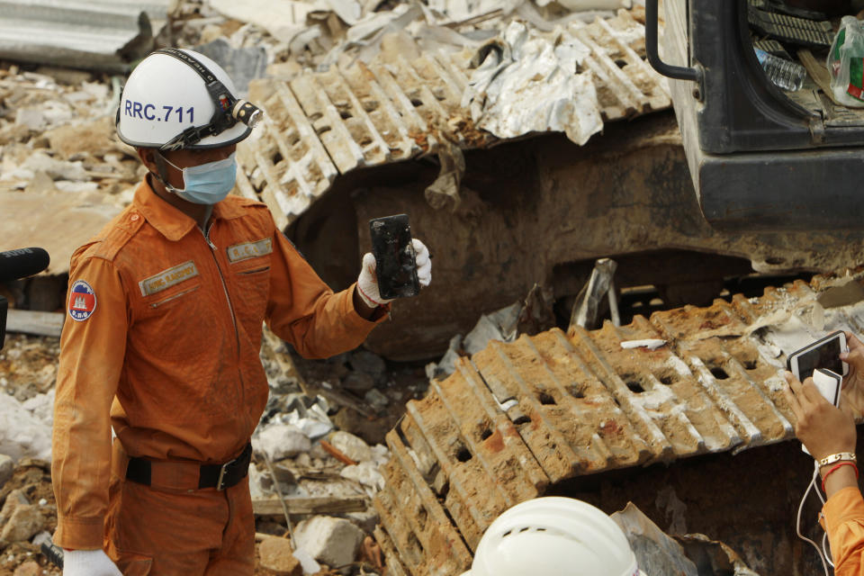 A rescuer shows a smart phone found from the rubble at the site of a collapsed building and possibly belonging to one of the victims, in Preah Sihanouk province, Cambodia, Sunday, June 23, 2019. Rescue workers were using saws to cut steel beams and excavators to move piles of rubble of the collapsed seven-story building. (AP Photo/Heng Sinith)