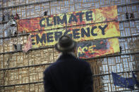 A man looks up as police and fire personnel move in to remove climate activists after they climbed the Europa building during a demonstration outside an EU summit meeting in Brussels, Thursday, Dec. 12, 2019. Greenpeace activists on Thursday scaled the European Union's new headquarters, unfurling a huge banner warning of a climate emergency hours before the bloc's leaders gather for a summit focused on plans to combat global warming.(AP Photo/Francisco Seco)