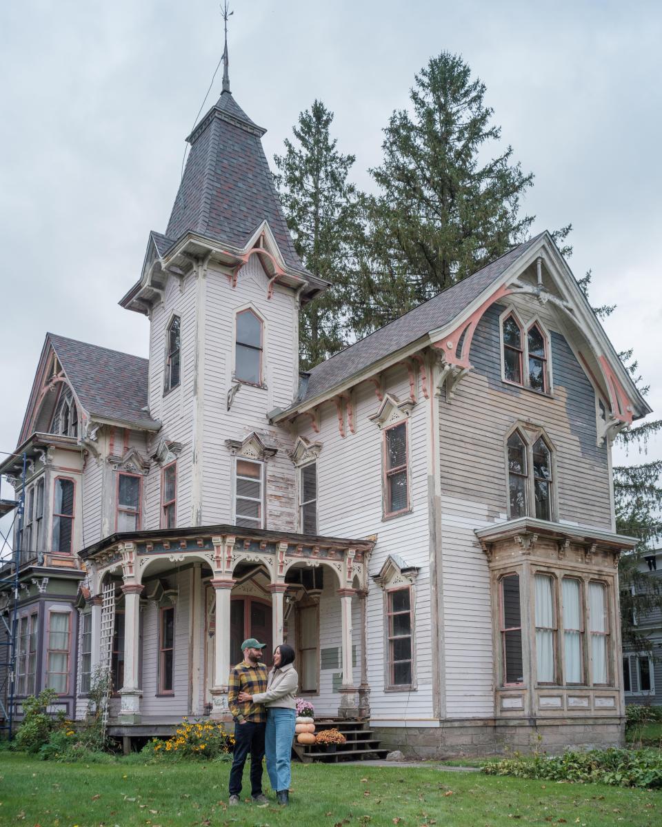 A couple stands in front of their Victorian home.