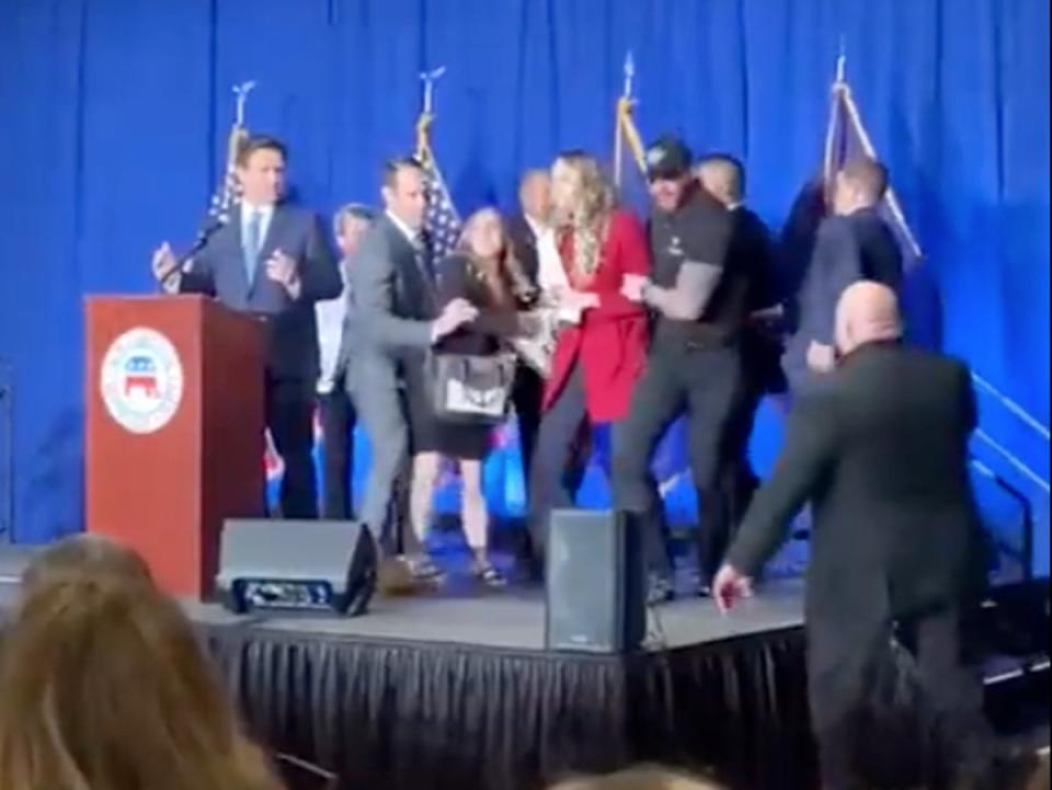 A pair of protesters from IfNotNow are led off-stage by security at a Republican fundraiser event in New Hampshire as Florida Governor Ron DeSantis watches from the podium (Screengrab/IfNotNow)