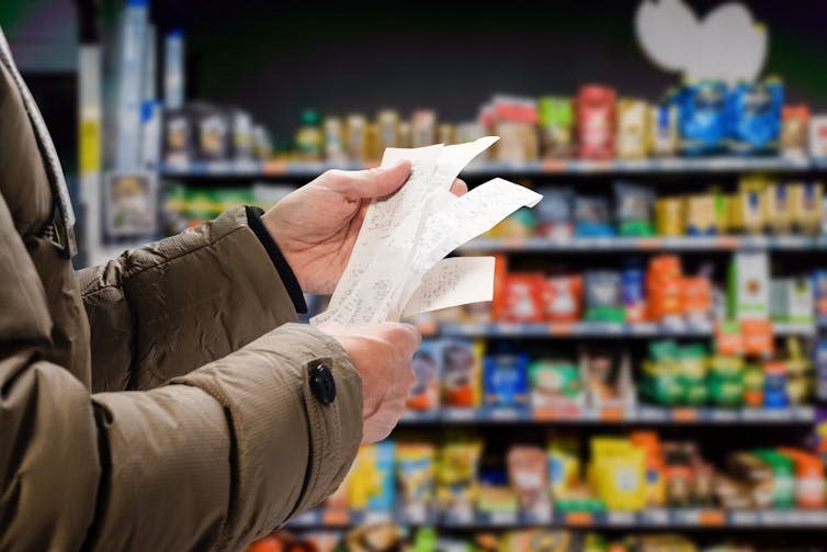 Close up of a man's hands holding receipts while shopping in a supermarket