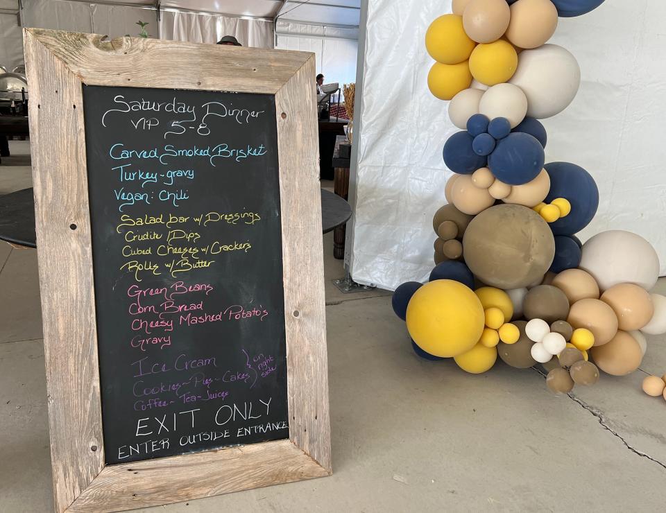 A chalkboard menu with colorful writing on it next to the bottom of an arch of yellow and blue balloons
