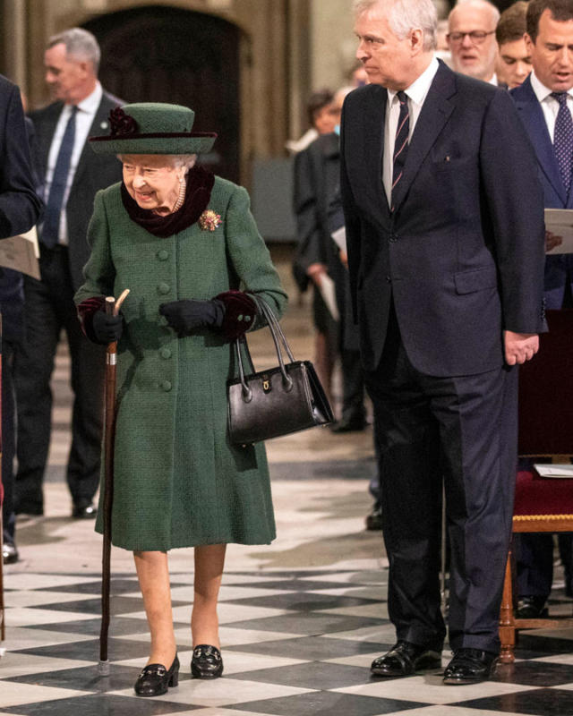 The Queen attends an event in a green outfit and green hat, using a walking stick. 