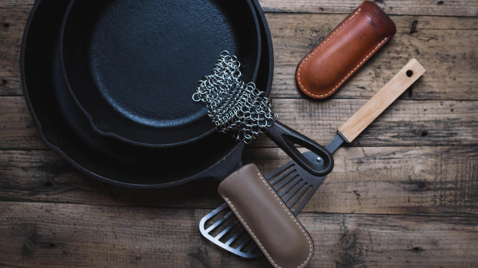 A cast iron skillet next to a spatula and metal scrubber