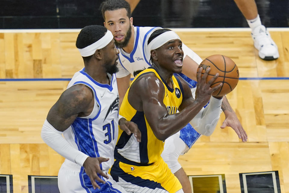 Indiana Pacers guard Aaron Holiday, right, shoots as he gets past Orlando Magic guards Terrence Ross, left, and Michael Carter-Williams during the first half of an NBA basketball game, Friday, April 9, 2021, in Orlando, Fla. (AP Photo/John Raoux)