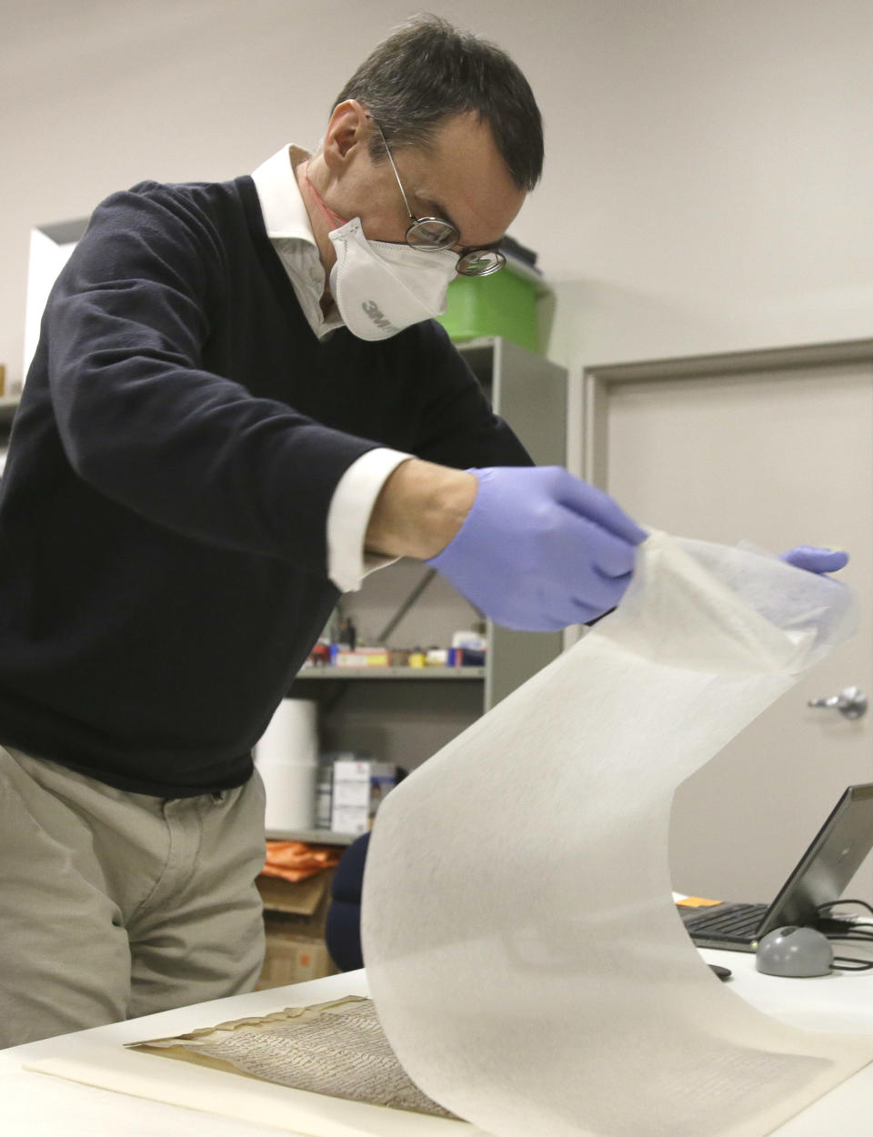 In this Wednesday, Feb. 5, 2014 photo, wearing gloves and a mask, Chris Woods, director of London's National Conservation Service, very carefully unveils the Magna Carta, in Houston. The centuries old parchment will be on display at the Houston Museum of Natural Science for six months starting Feb. 14, 2014. (AP Photo/Pat Sullivan)