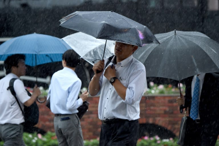 Businessmen walk under heavy rain in downtown Tokyo on August 22, 2016 as Typhoon Mindulle strikes the region