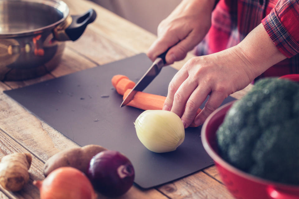 Cooking at home - Vegetable soup preparing, female hand holding kitchen knife, chopping carrot and onions