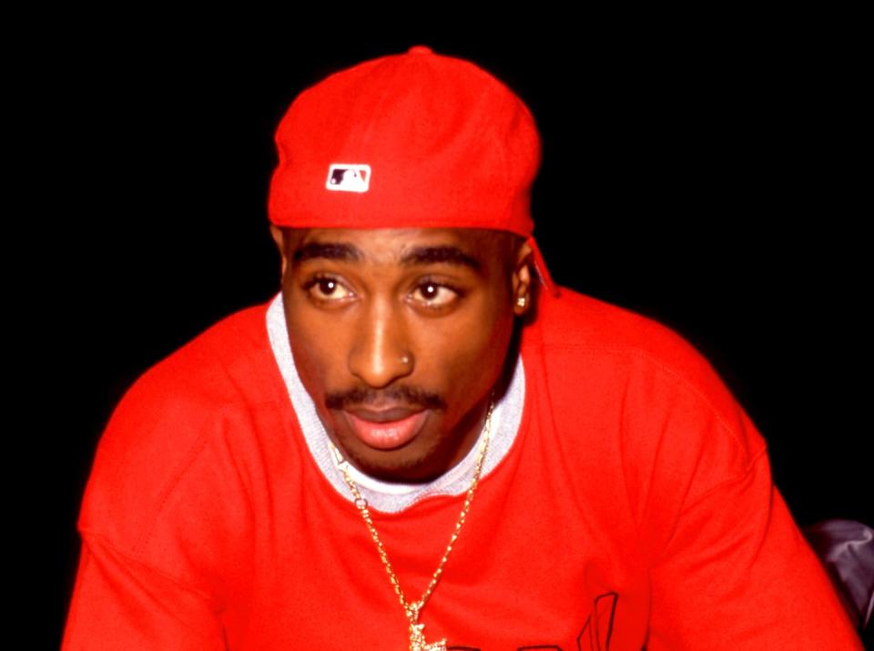 tupac shakur, wearing a red shirt, gold chain, and backwards red hat