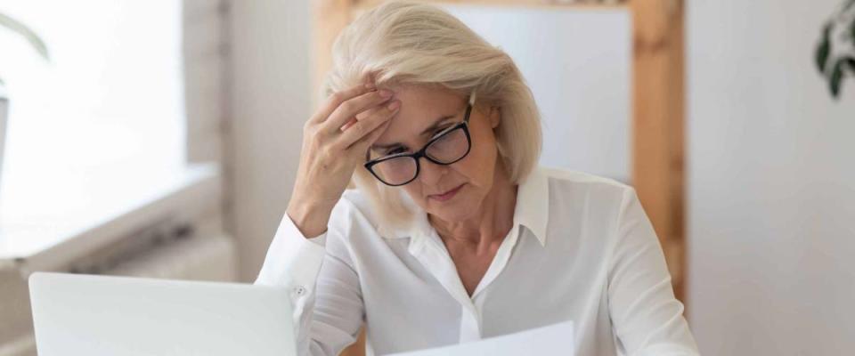 Woman looking at sheet of paper while holding her head, looking concerned