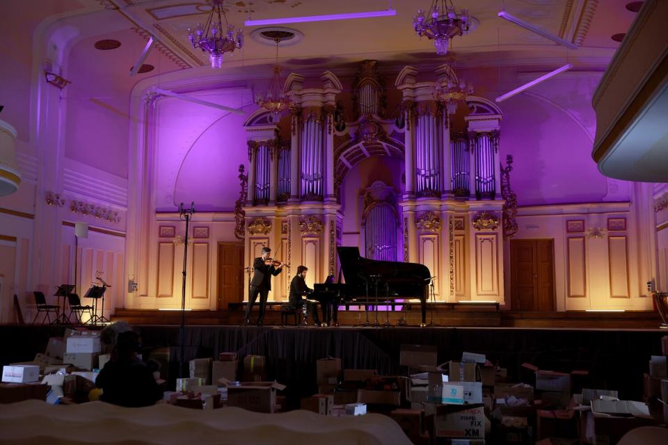 A pianist and violinist on a stage lighted in blue and yellow, the colors of Ukraine's flag