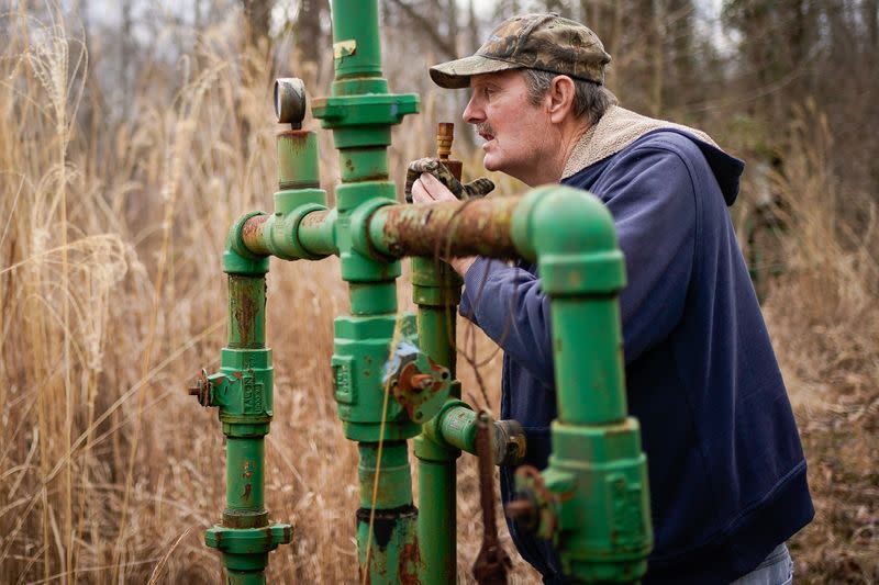 Hanson Rowe, a landowner who blames a leaky gas well on his property for health problems, smells for the odor of gas emanating from an abandoned well on his property in Salyersville