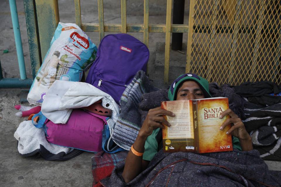 Luis Rene Reyes Garcia, 28, of Guatemala, reads a donated bible as he rests on the street outside of a sports complex where more than 5,000 Central Americans are sheltering, in Tijuana, Mexico, Wednesday, Nov. 28, 2018. "At home I drank a lot, but now I've quit," said Reyes. "I am getting closer to god." Reyes, who worked in banana packing in Guatemala, said he joined the caravan to find a way to earn money to support his daughter back home. (AP Photo/Rebecca Blackwell)