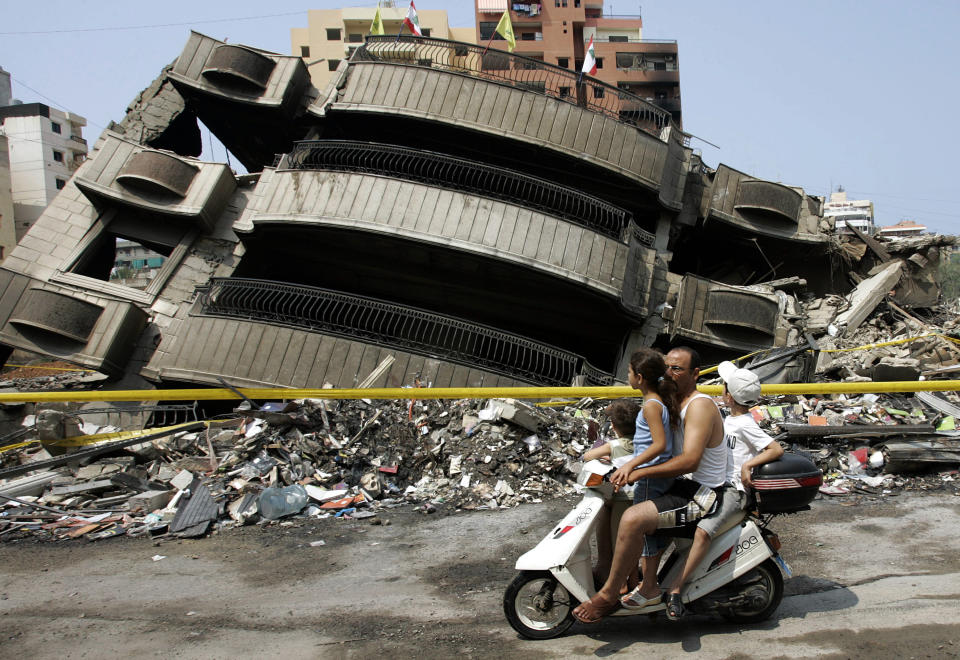 File - In this August 20, 2006 file photo, a Lebanese man with his three children, riding a scooter pass in front of a destroyed building that was attacked during the 34-day long Hezbollah-Israeli war, in the Hezbollah stronghold in the southern suburbs of Beirut, Lebanon. Lebanon's Hezbollah militia looms large over the current Israel-Hamas war, even though it has stayed out of the fighting so far. Hezbollah's firepower is far greater than that of Gaza's Hamas rulers, and Israel keeps a wary eye on its northern border for any signs Hezbollah might get off the sidelines. (AP Photo/Hussein Malla, File)