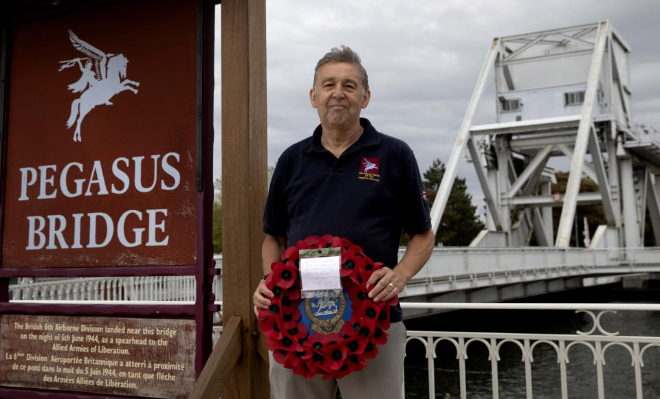 In this photo taken on Friday, June 5, 2020, British expatriate Steven Oldrid holds a poppy wreath as he stands on the site of the original WWII Pegasus Bridge in Benouville, Normandy, France. Due to coronavirus measures many relatives and veterans will not make this years 76th anniversary of D-Day. Oldrid will be bringing it to them virtually as he places wreaths and crosses for families and posts the moments on his facebook page. (AP Photo/Virginia Mayo)