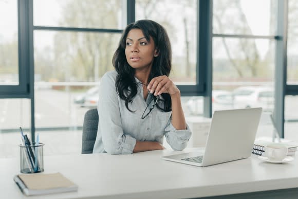 Businesswoman sits at a desk looking pensive.