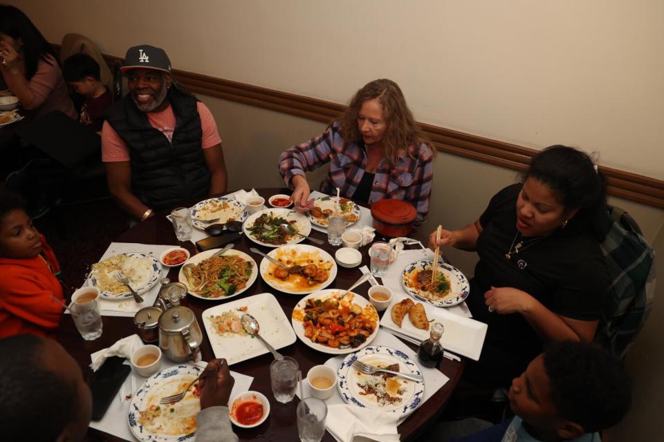 A family eating dinner around a round table covered with plates full of food.