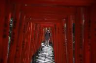 Man wearing protective face mask walks through red-coloured wooden torii gates at the Nezu shrine in Tokyo