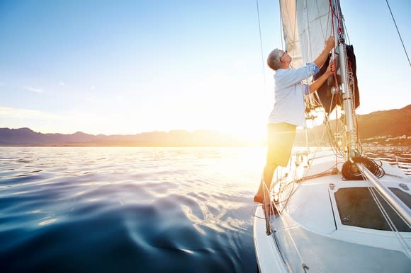 Man fixing the sail on a sailboat that's on open waters.