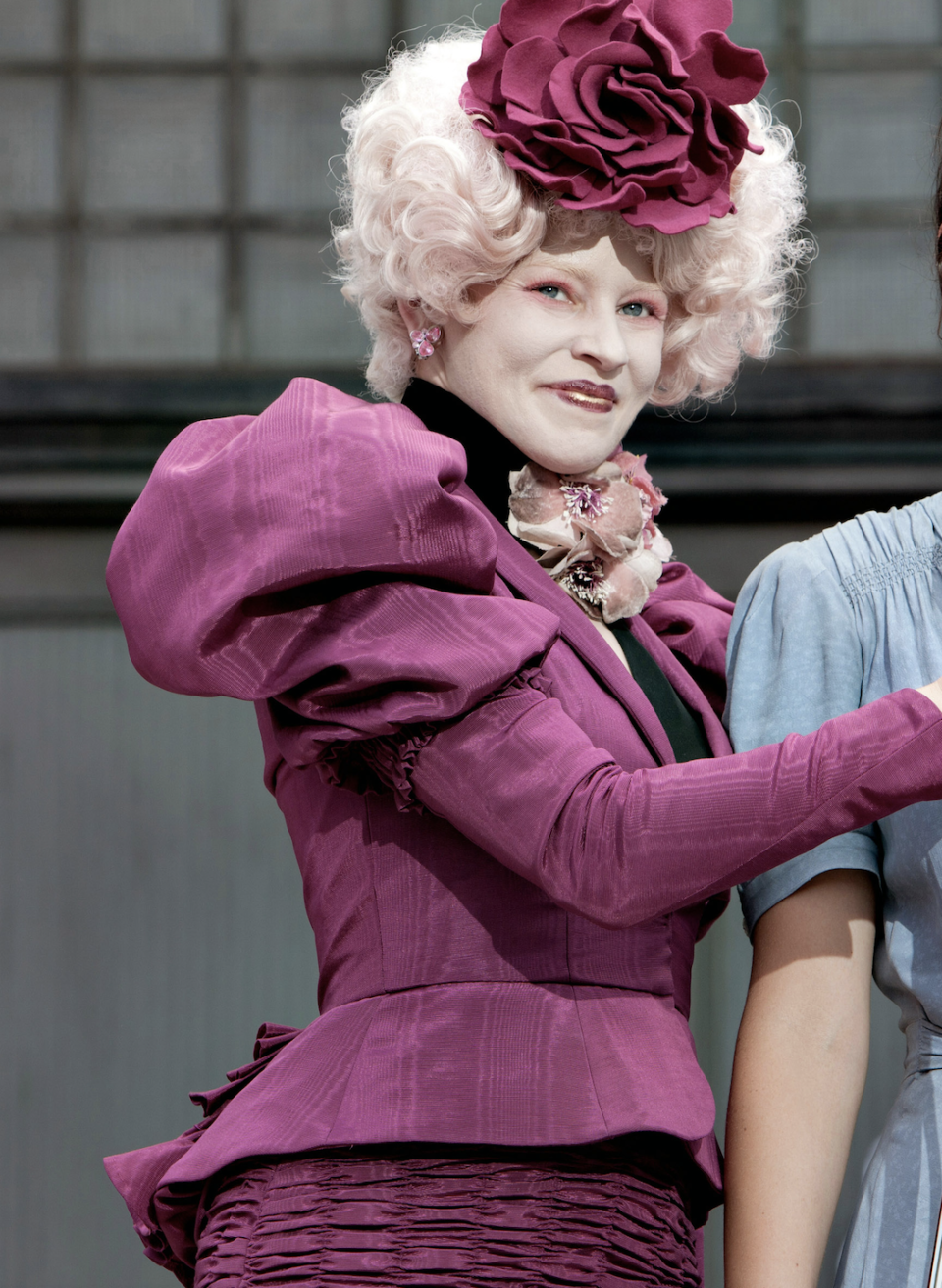 Effie Trinket from The Hunger Games, wearing a ruffled magenta dress with matching hat