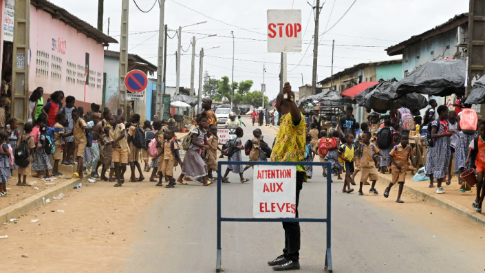A lollipop man oversees schoolchildren crossing a road in Abidjan, Ivory Coast - Wednesday 16 March 2022