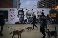 People walk past a graffiti depicting Spain's King Felipe VI, former King Juan Carlos and Spain's late dictator Francisco Franco by artist BlackBlock, in support of Catalan rap artist Pablo Hasel in Barcelona, Spain, Sunday, Feb. 21, 2021. The imprisonment of Pablo Hasel for inciting terrorism and refusing to pay a fine after having insulted the country's monarch has triggered a social debate and street protests. (AP Photo/Felipe Dana)