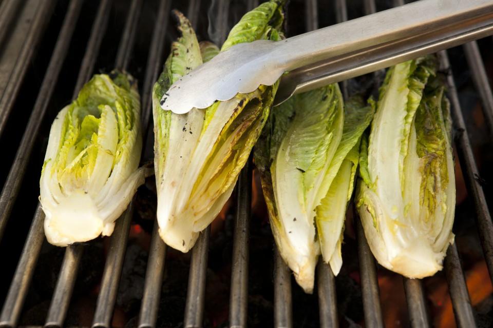 tongs turning heads of romaine lettuce on grill