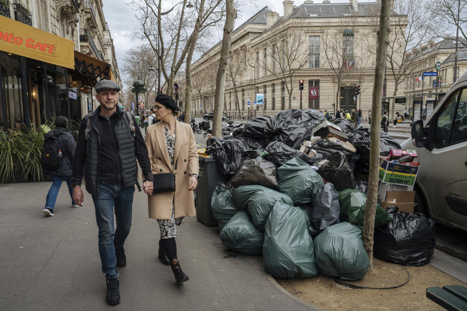 People walk past uncollected garbage in Paris, Monday, March 13, 2023. A contentious bill that would raise the retirement age in France from 62 to 64 got a push forward with the Senate's adoption of the measure amid strikes, protests and uncollected garbage piling higher by the day. (AP Photo/Lewis Joly)