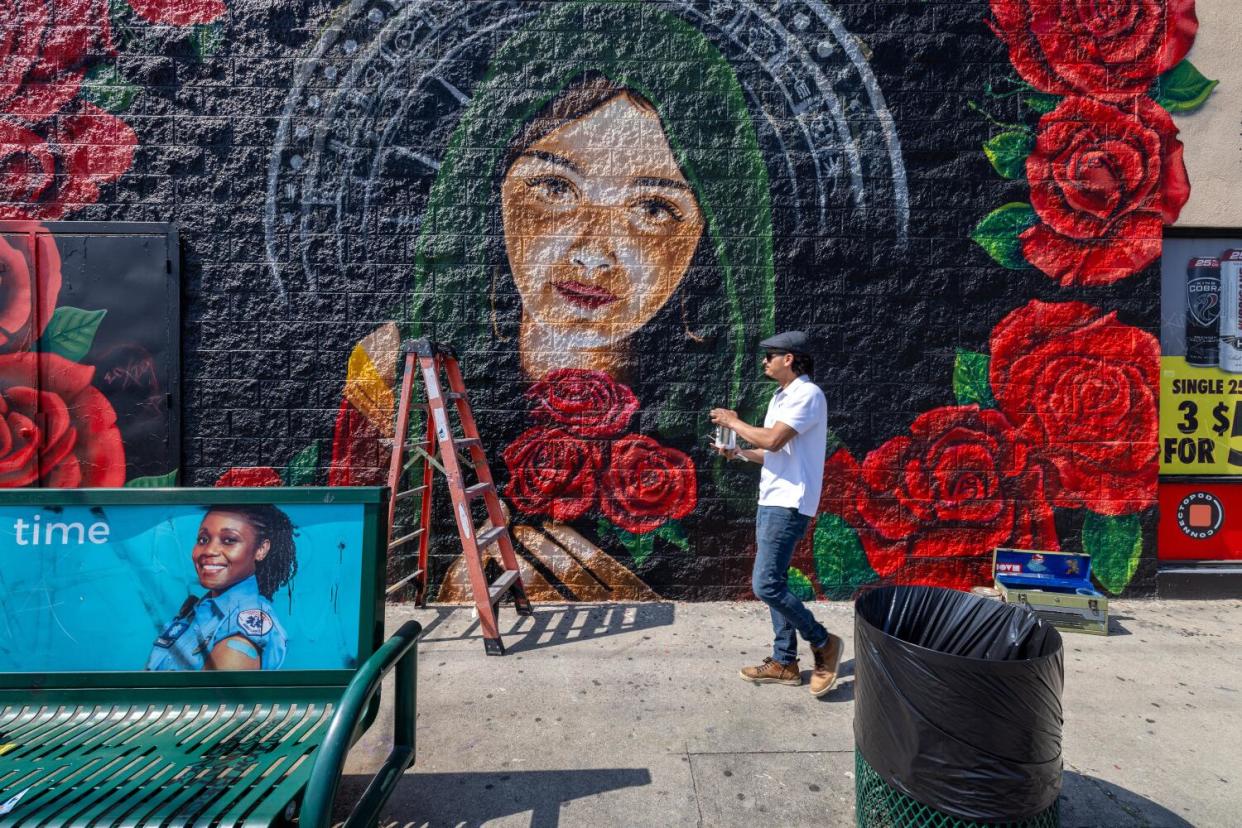 A man appears in front of a mural of a woman.