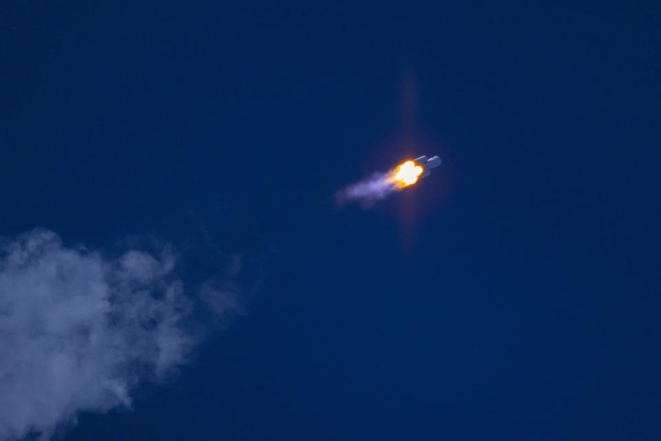 a large white rocket with four smaller boosters takes off above a plume of fire